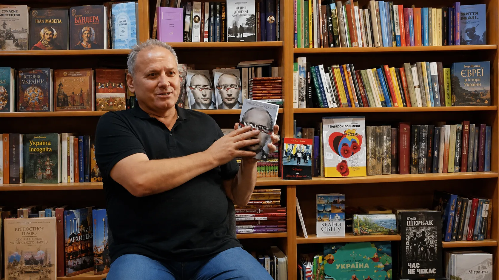 Богдан Кушнір у книгарні тримає книжку в руках, за спиною — стелажі з книжками
